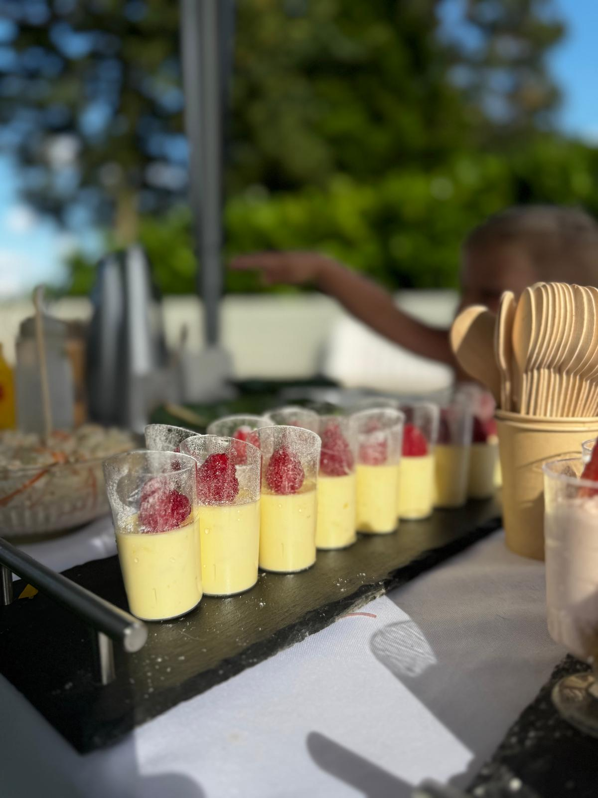 Row of individual posset pots with raspberries at an outdoor event